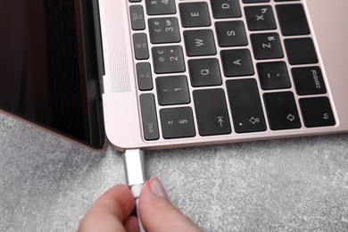 Woman plugging USB cable into laptop port at grey table, closeup