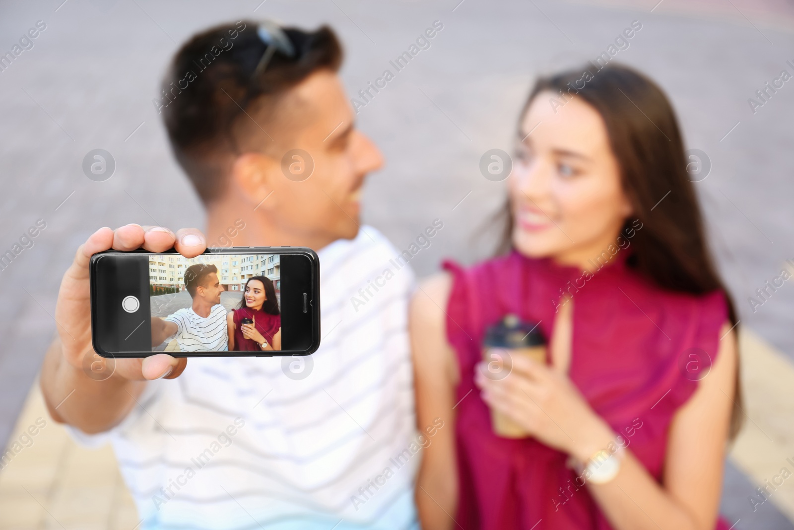 Photo of Young couple taking selfie outdoors, focus on smartphone