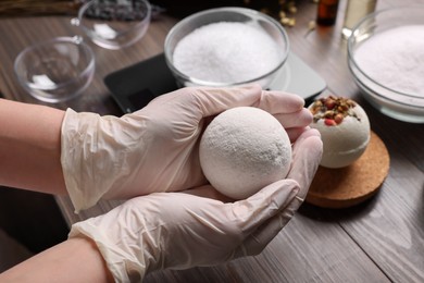 Photo of Woman holding handmade bath bomb above wooden table, closeup