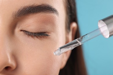 Young woman applying serum onto her face on light blue background, closeup