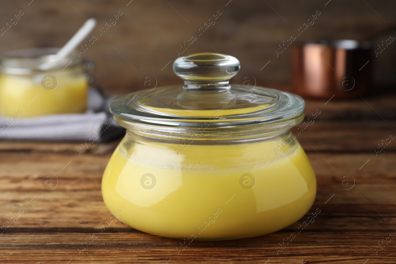 Photo of Glass jar of Ghee butter on wooden table, closeup