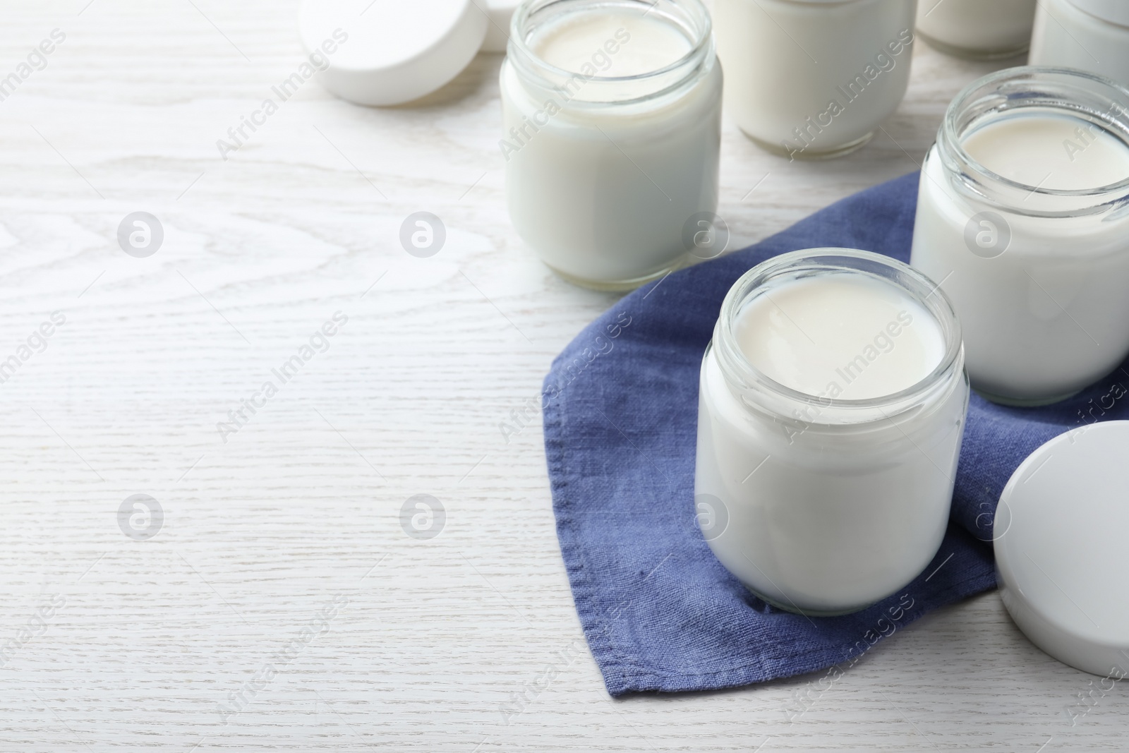 Photo of Tasty yogurt in glass jars on white wooden table. Space for text