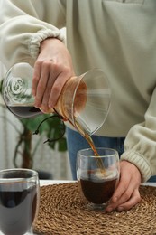 Woman pouring drip coffee from chemex coffeemaker into glass at table, closeup