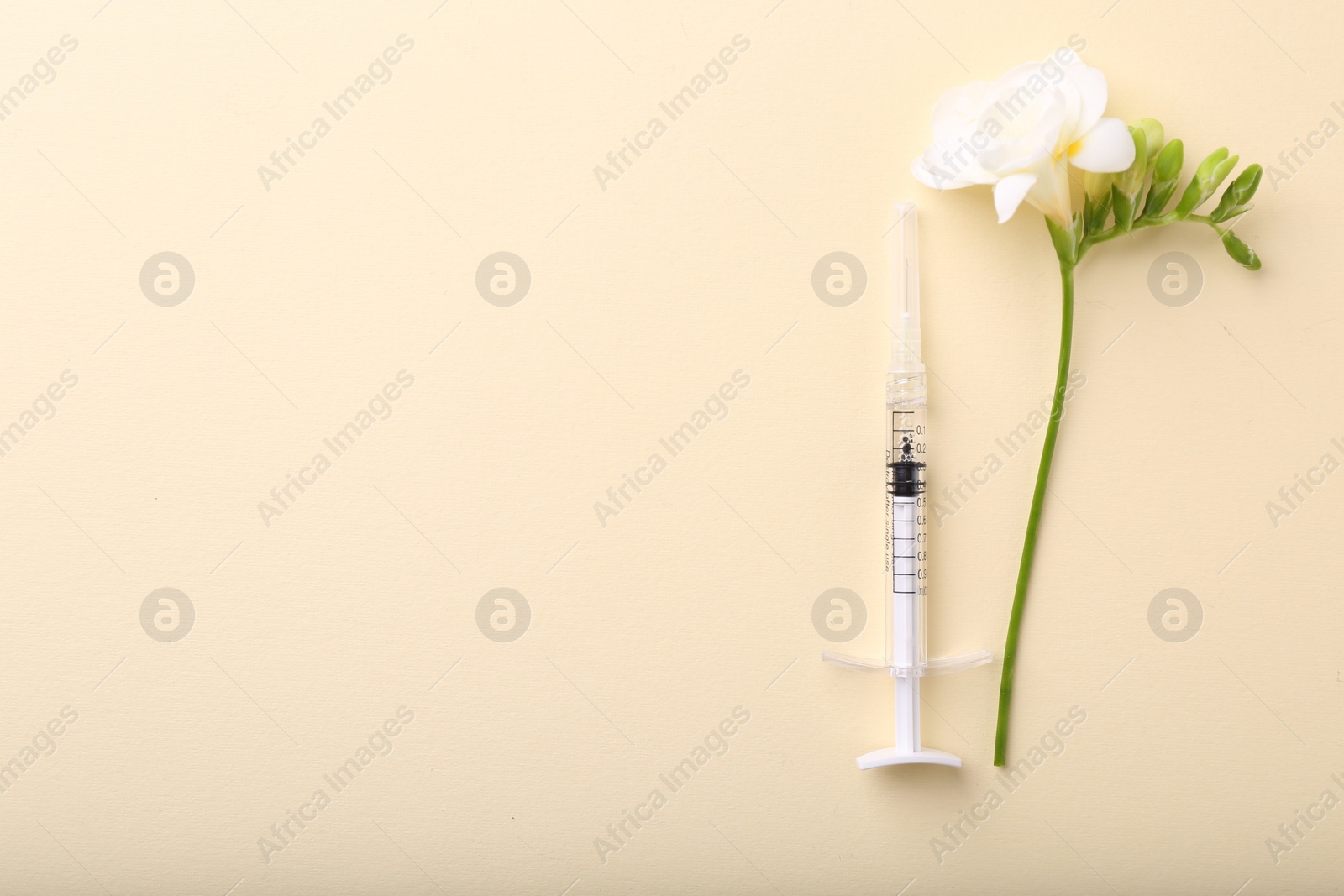 Photo of Cosmetology. Medical syringe and freesia flower on yellow background, flat lay. Space for text