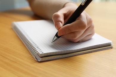 Left-handed woman writing in notebook at wooden desk, closeup