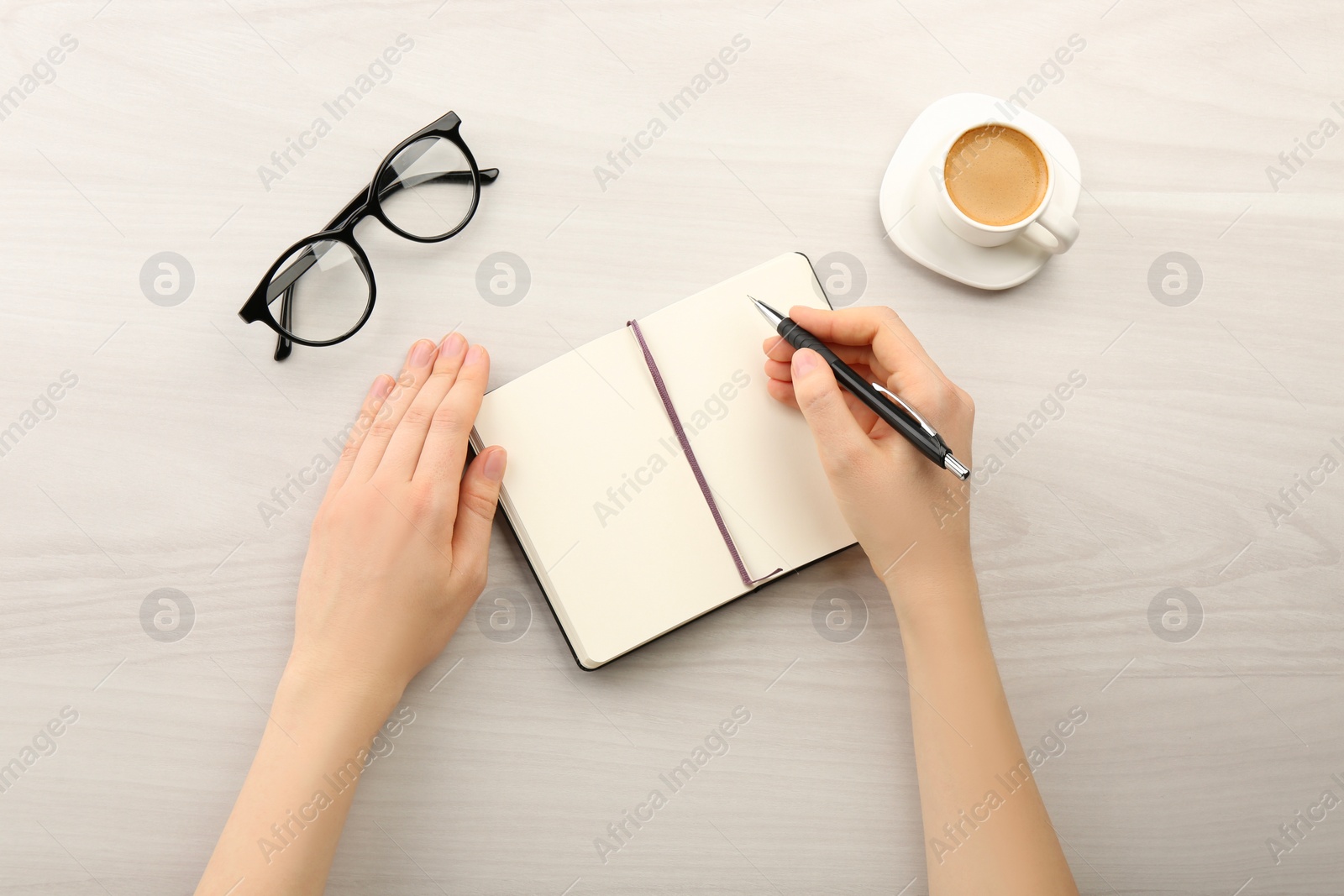 Photo of Woman writing in notebook at light wooden table, top view