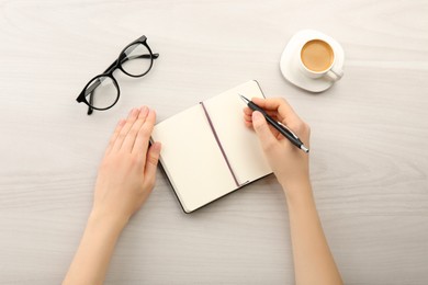 Photo of Woman writing in notebook at light wooden table, top view