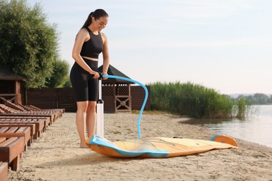 Woman pumping up SUP board on river shore