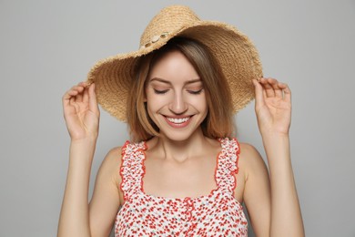 Beautiful young woman wearing straw hat on light grey background. Stylish headdress