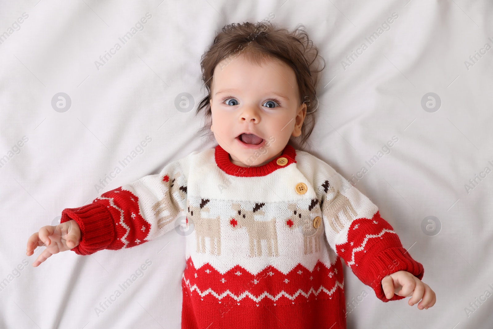 Photo of Cute little baby in Christmas sweater on soft bed, top view