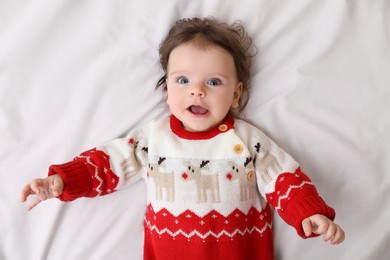 Photo of Cute little baby in Christmas sweater on soft bed, top view