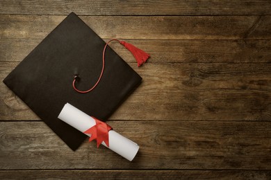 Image of Graduation hat and diploma on wooden table, flat lay. Space for text