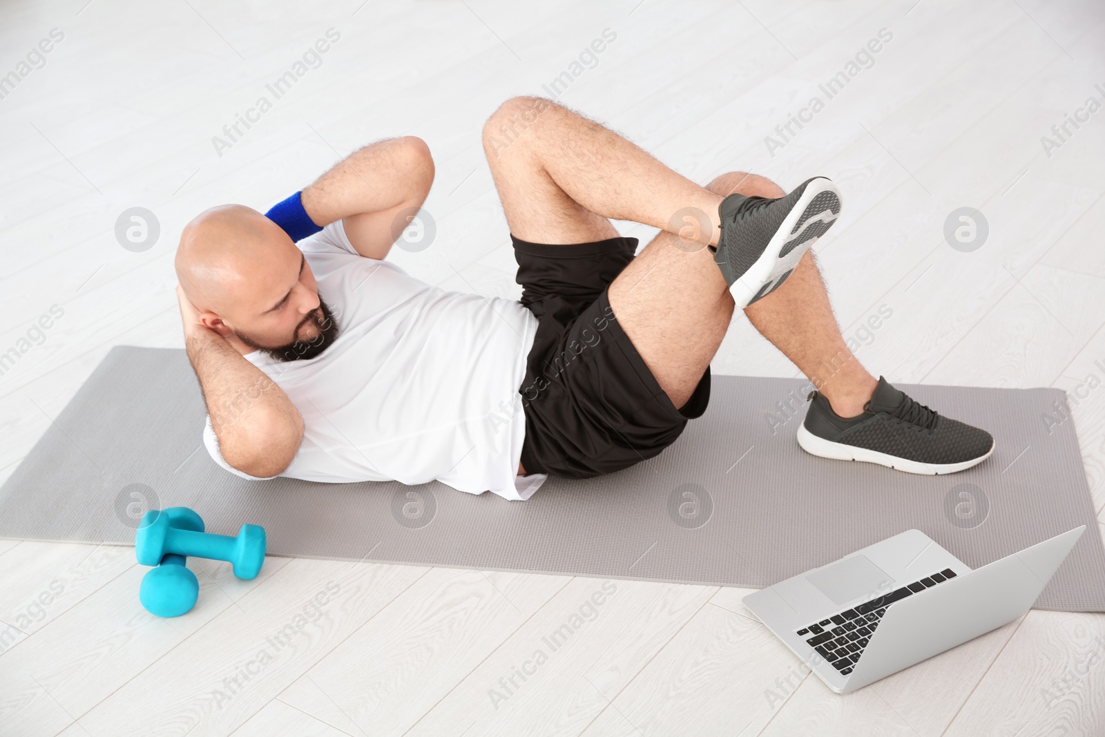 Photo of Overweight man doing exercise while watching tutorial on laptop at home