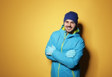 Young man wearing warm clothes on color background, space for text. Ready for winter vacation