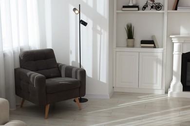 Photo of Armchair and floor lamp near stylish shelves with different decor elements in room. Interior design