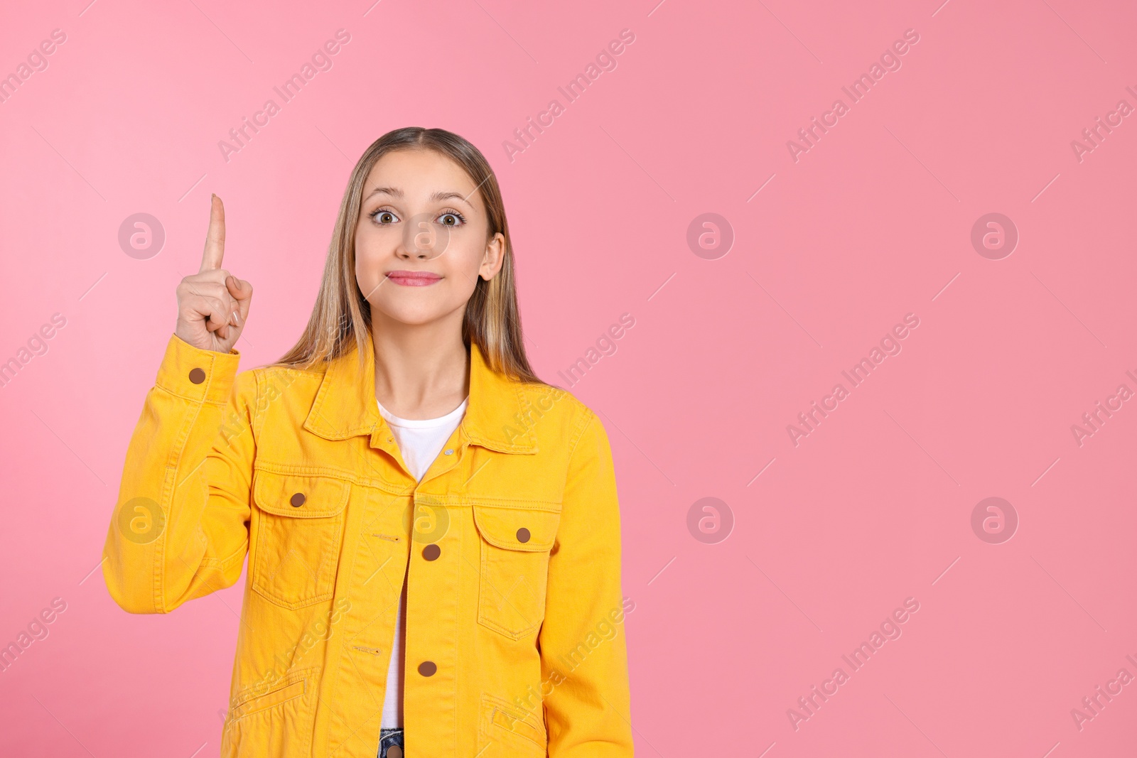 Photo of Beautiful teenage girl pointing at something on pink background. Space for text