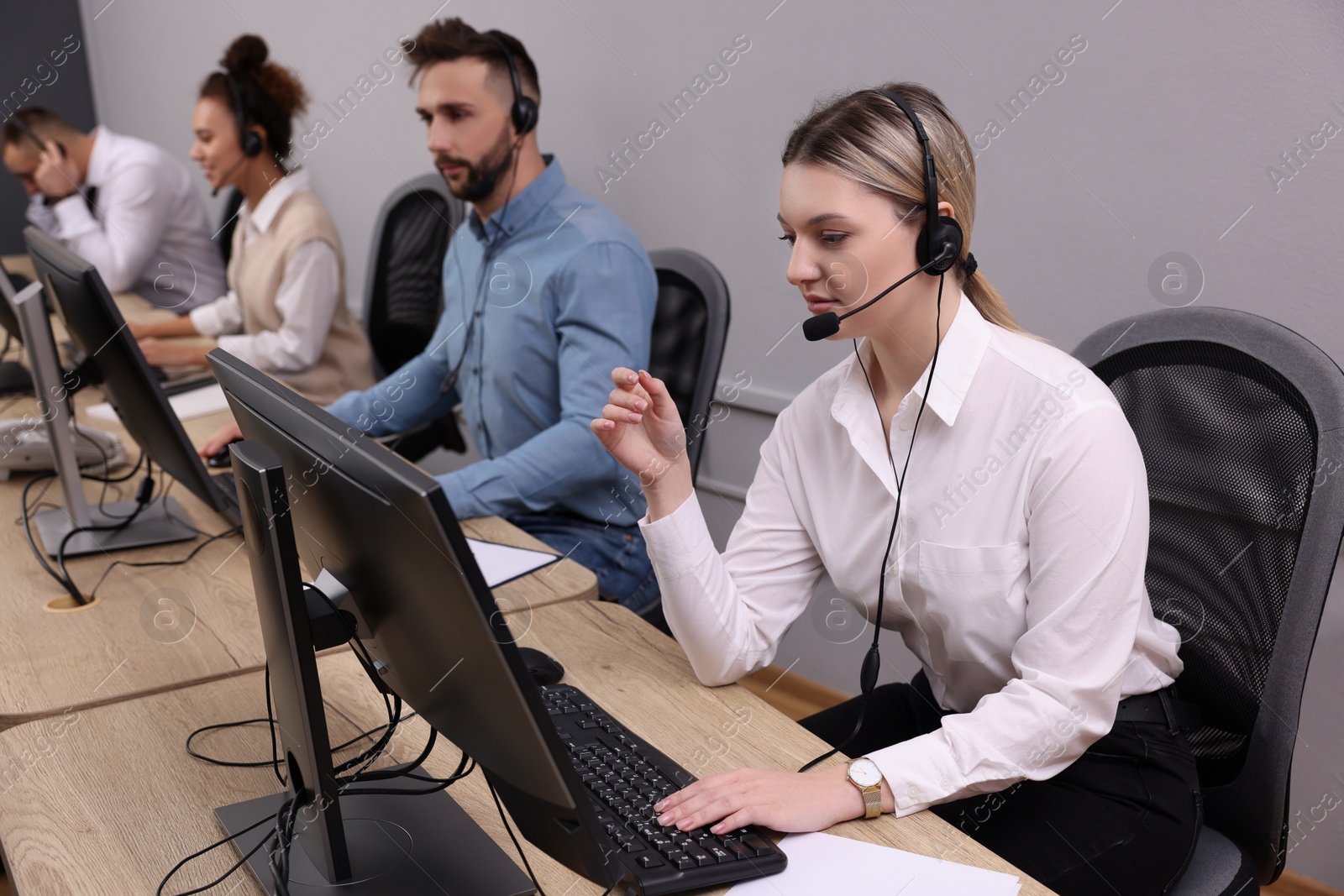 Photo of Call center operators working in modern office, focus on young woman with headset