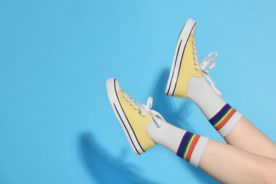 Photo of Woman posing in yellow classic old school sneakers on light blue background, closeup. Space for text