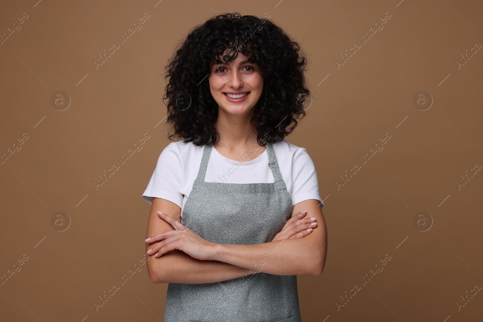 Photo of Happy woman wearing kitchen apron on brown background. Mockup for design