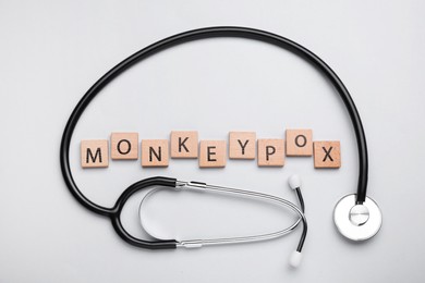 Photo of Word Monkeypox made of wooden cubes and stethoscope on light background, flat lay