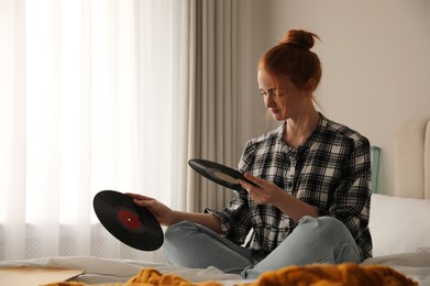 Photo of Young woman choosing vinyl disc to play music with turntable in bedroom