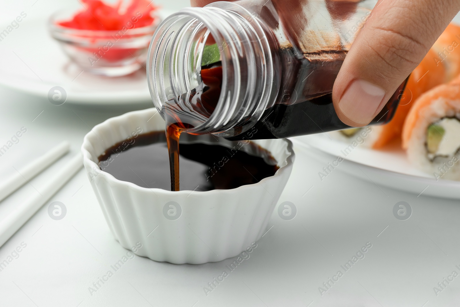 Photo of Woman pouring tasty soy sauce into bowl at white marble table, closeup