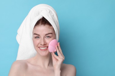 Washing face. Young woman with cleansing brush on light blue background, space for text