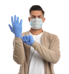 Man in protective face mask putting on medical gloves against white background