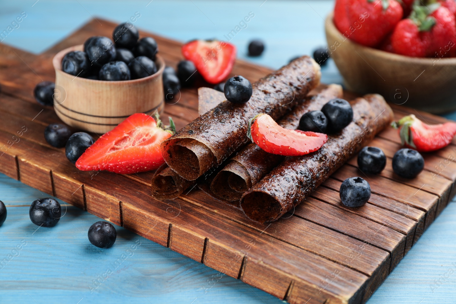 Photo of Delicious fruit leather rolls and berries on light blue wooden table, closeup