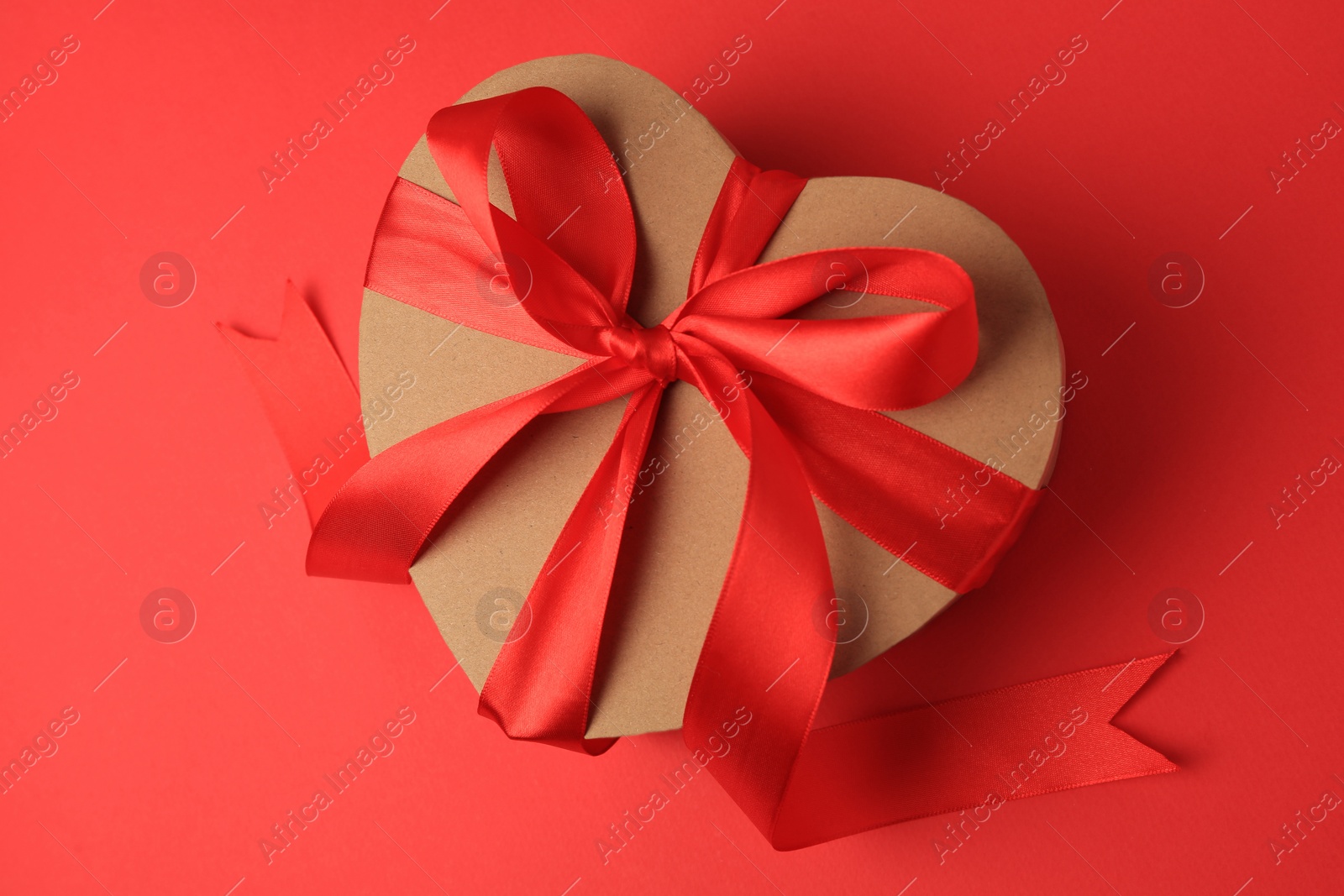 Photo of Beautiful heart shaped gift box with bow on red background, top view