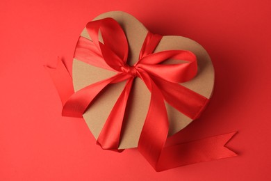 Beautiful heart shaped gift box with bow on red background, top view