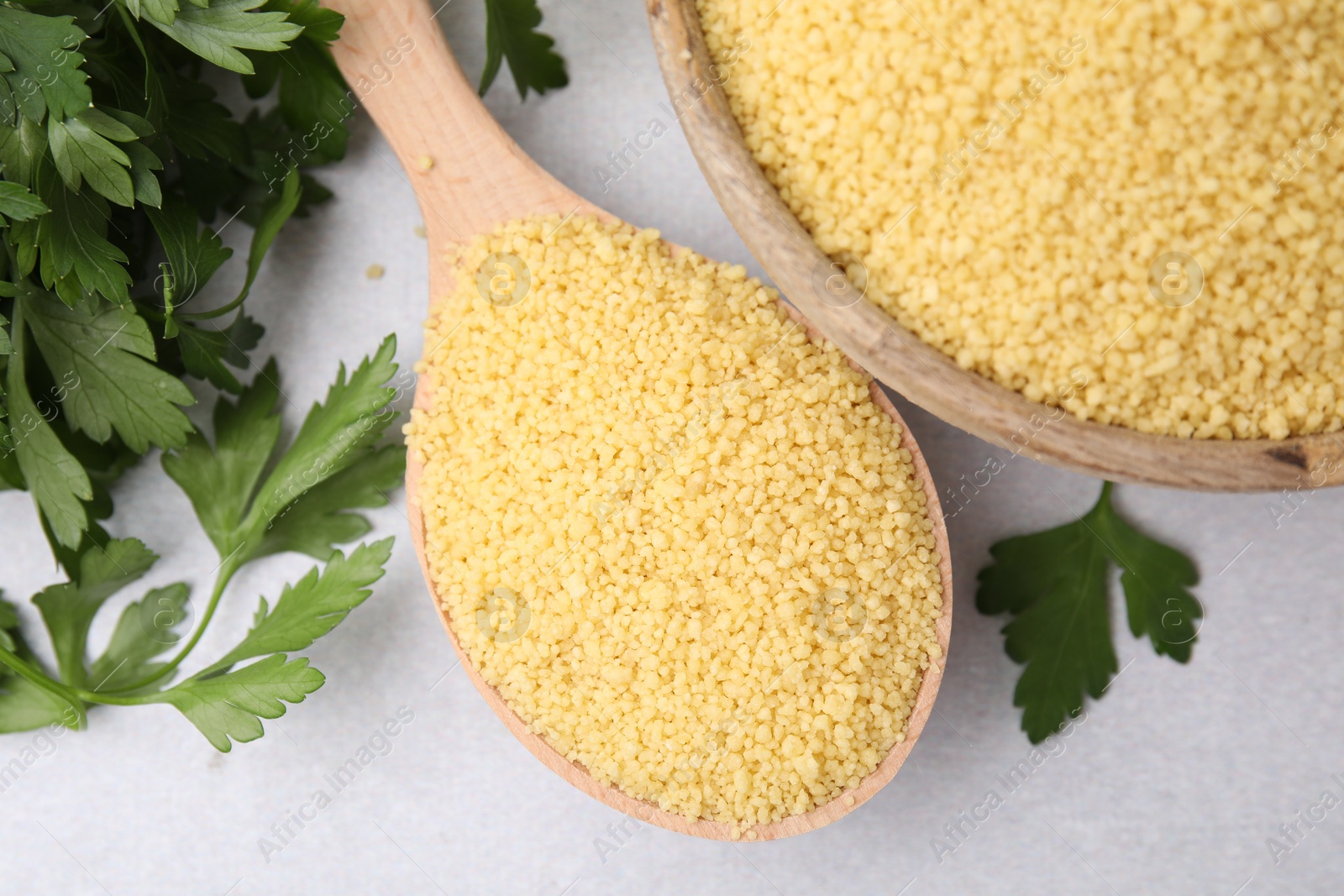 Photo of Raw couscous in bowl, spoon and parsley on light table, flat lay