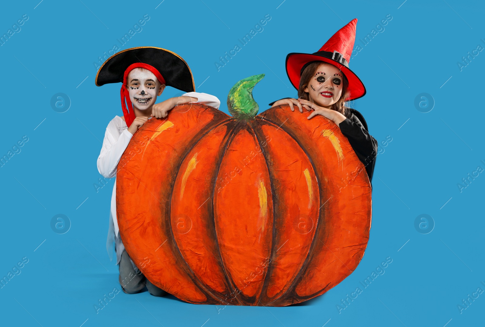 Photo of Cute little kids with decorative pumpkin wearing Halloween costumes on light blue background