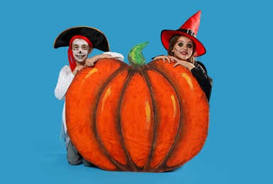 Cute little kids with decorative pumpkin wearing Halloween costumes on light blue background