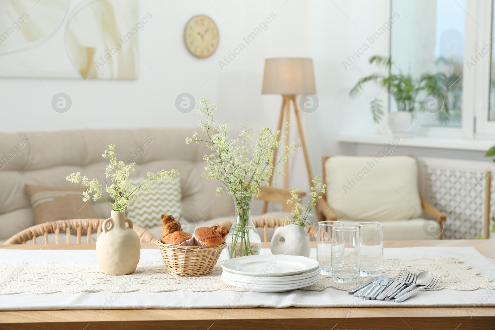 Photo of Clean dishes, flowers and fresh pastries on table in stylish dining room