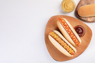 Photo of Tasty hot dogs with ketchup and mustard on white table, flat lay. Space for text