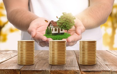 Stack of coins on wooden table and man holding house model. Real estate investing