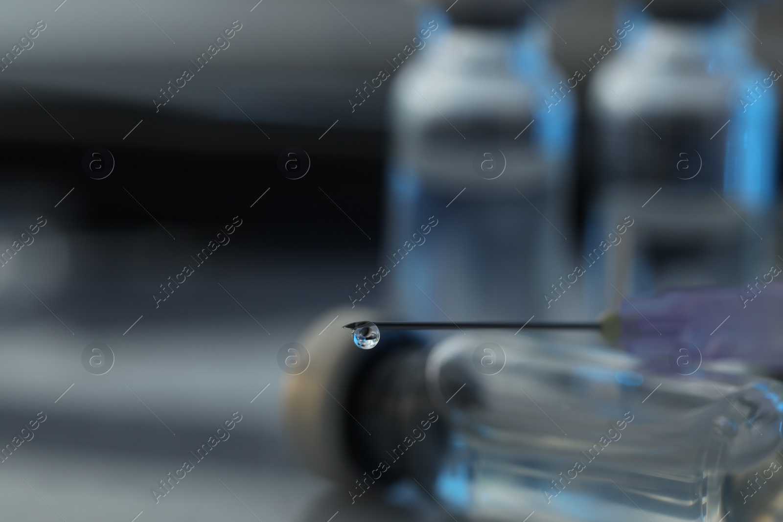 Photo of Drop of medication on syringe needle against blurred background, closeup. Space for text