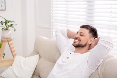 Photo of Handsome man relaxing on sofa at home, space for text