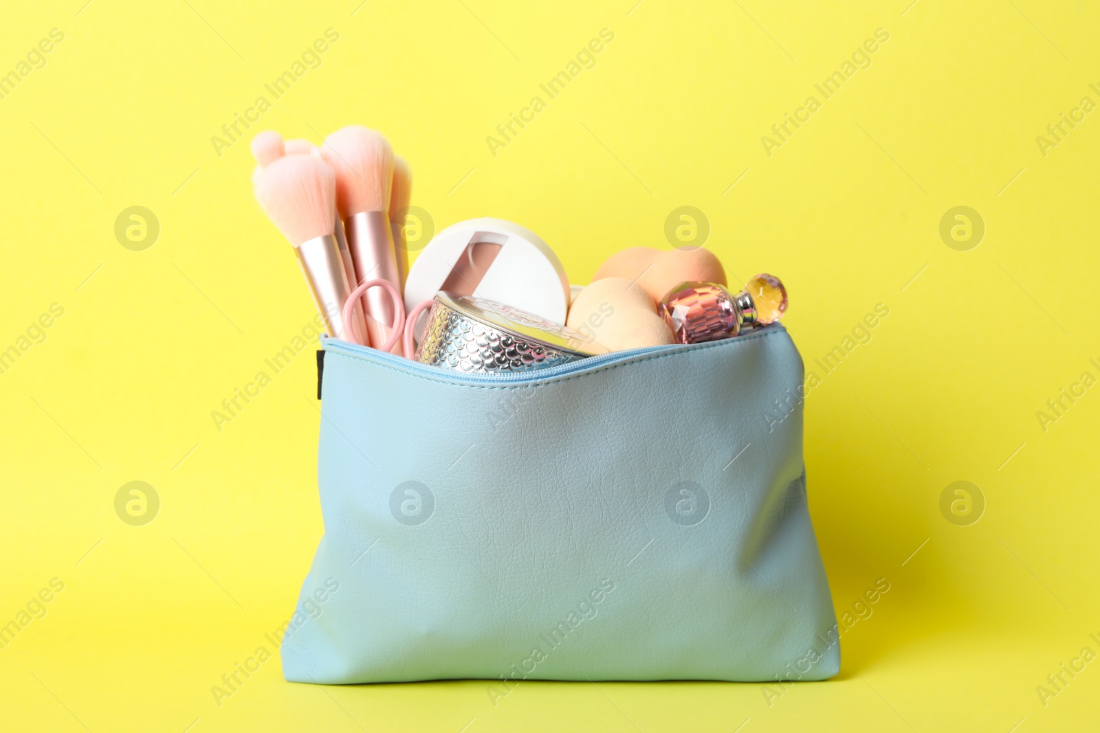 Photo of Cosmetic bag with makeup products and beauty accessories on yellow background