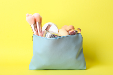 Cosmetic bag with makeup products and beauty accessories on yellow background