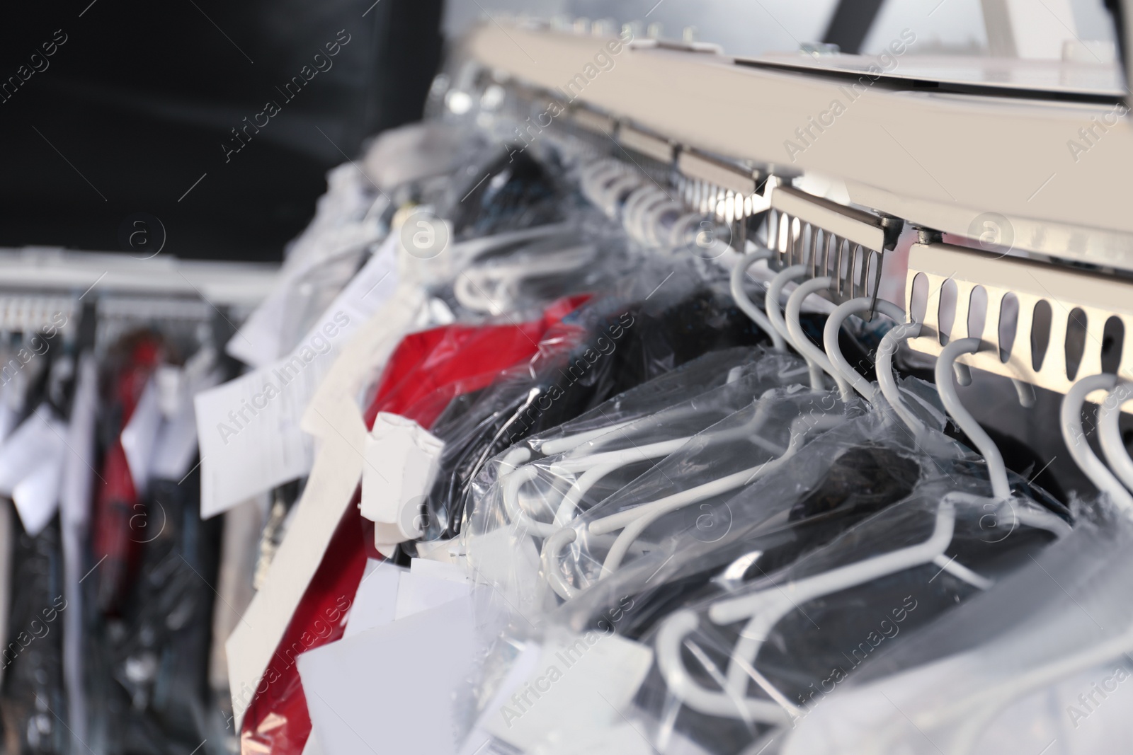 Photo of Hangers with clothes on garment conveyor at dry-cleaner's, closeup