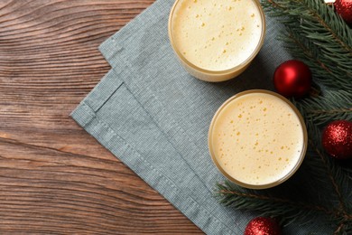 Photo of Glasses of delicious eggnog and decorated fir branch on wooden table, flat lay. Space for text