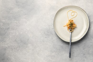 Photo of Heart made with spaghetti and fork on grey table, top view. Space for text