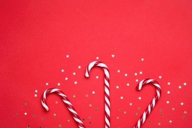 Photo of Delicious Christmas candy canes and confetti on red background, flat lay. Space for text