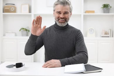 Photo of Man waving hello during video chat at home, view from webcam