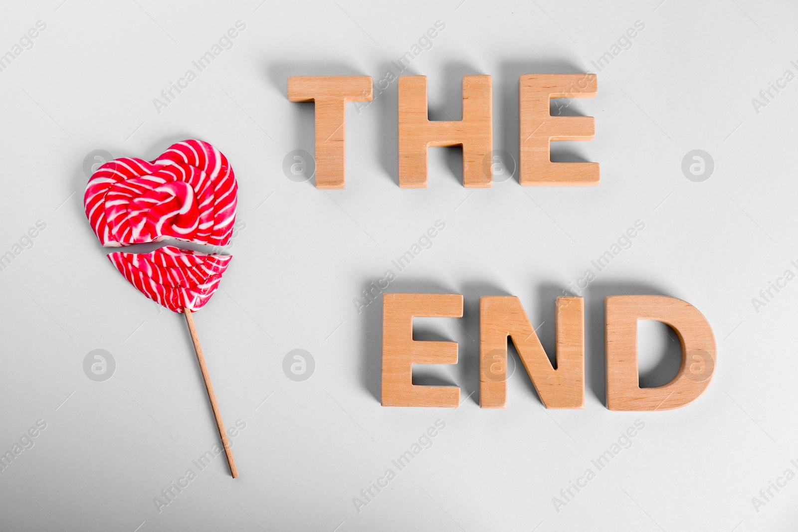 Photo of Broken heart shaped lollipop and phrase THE END made of wooden letters on white background, top view