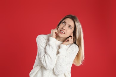 Photo of Emotional young woman covering her ears with fingers on red background