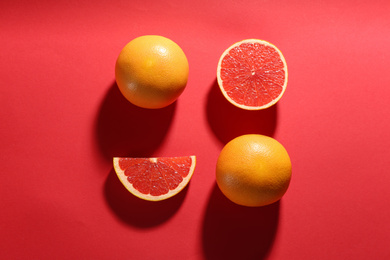 Cut and whole ripe grapefruits on red background, flat lay