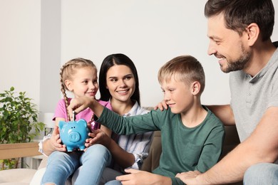 Photo of Happy family putting money into piggy bank at home